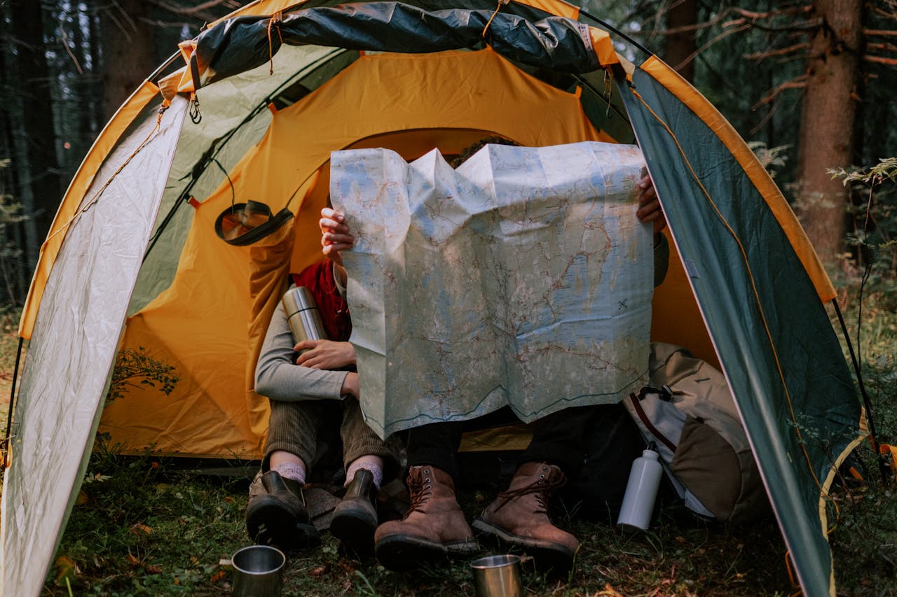 services-01 Two people enjoy a camping trip, examining a map inside a tent surrounded by nature.