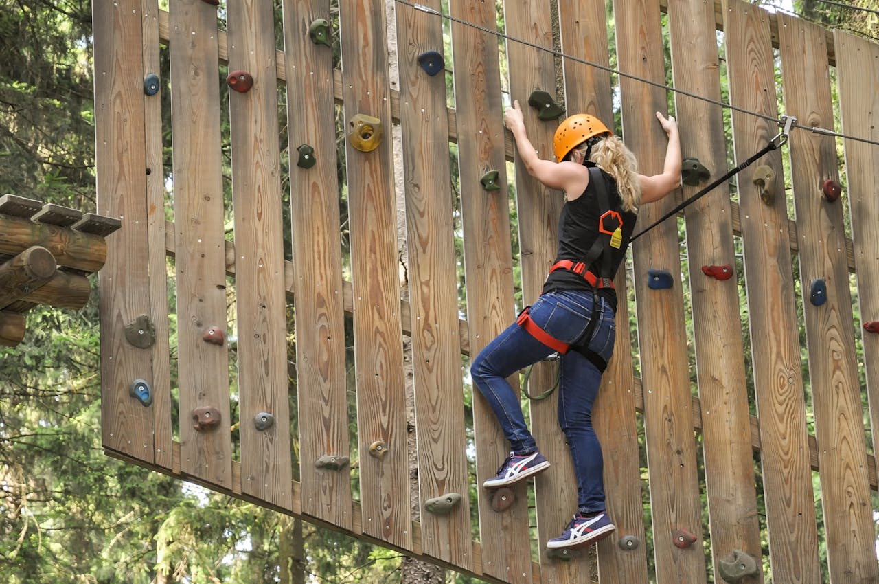 about-01 Woman climbing an outdoor adventure park wall with safety harness in Holzminden, Germany.